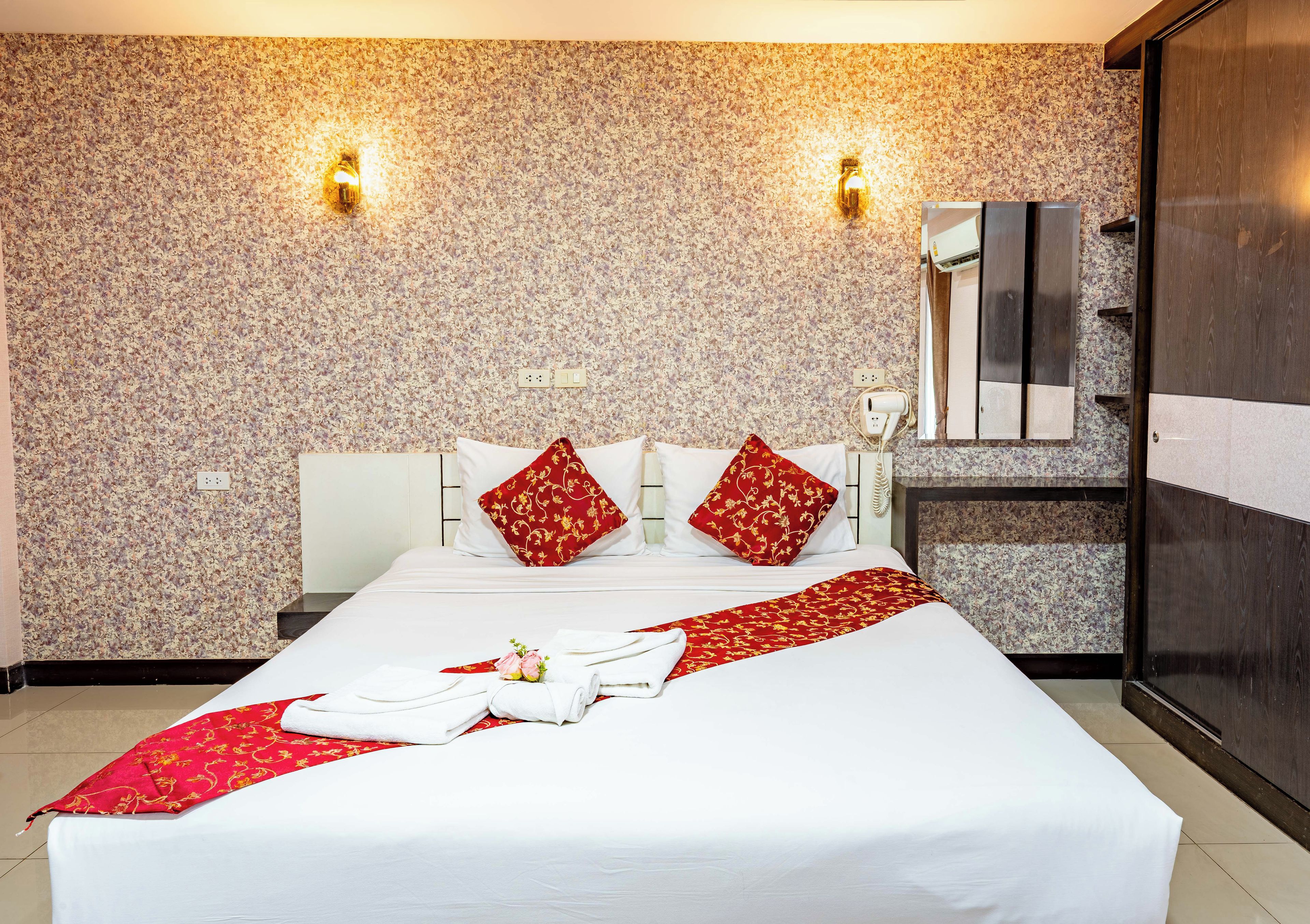 A hotel room with a large bed, two wall-mounted lights, a mirror, and a wardrobe.