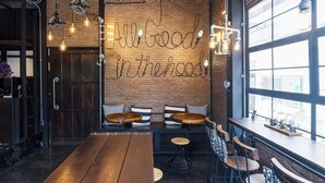 Un accogliente interno di un caffè con parete in mattoni, tavoli di legno e lo slogan 'All Good in the hood'.