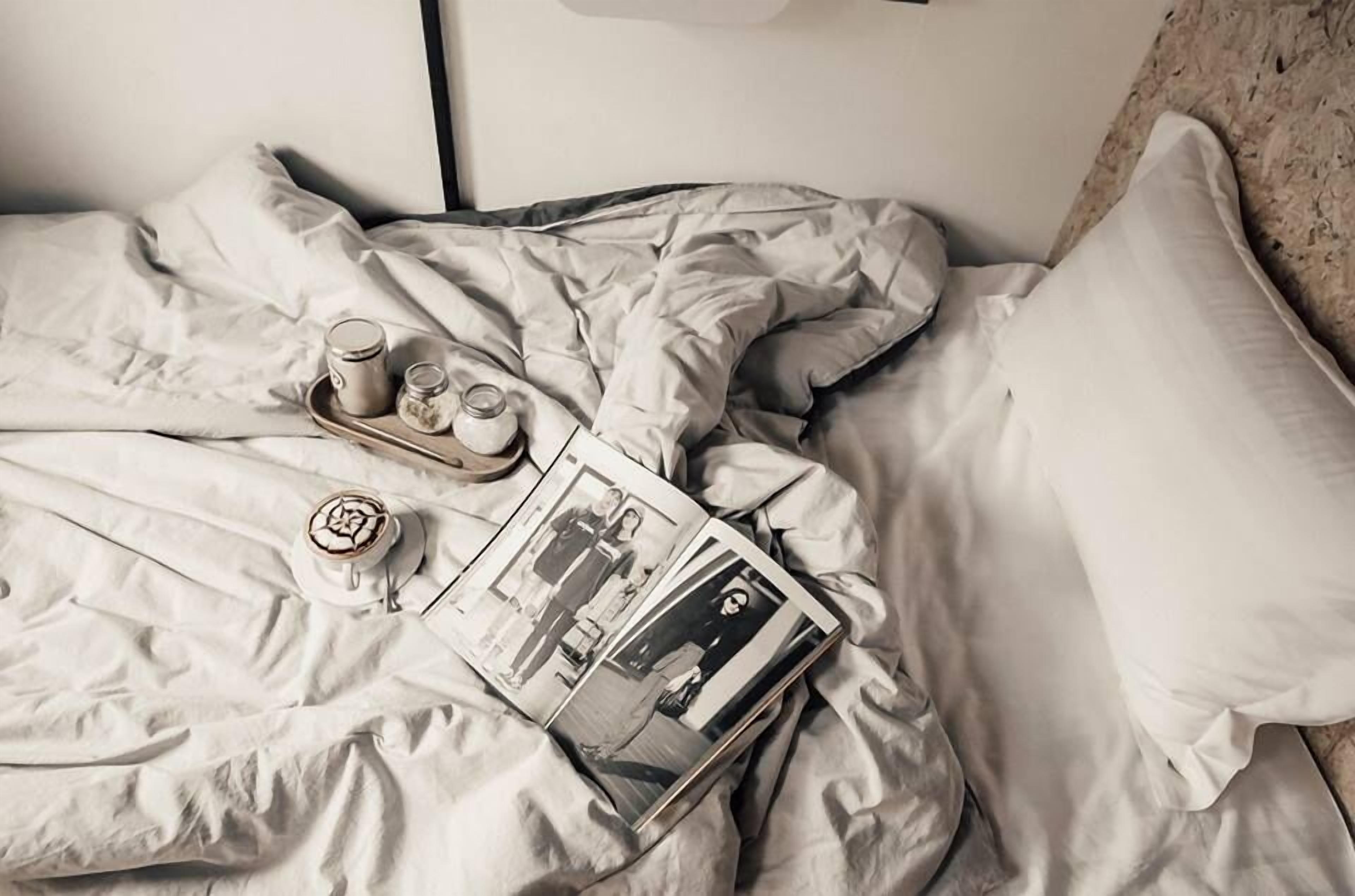 A bed with a magazine, a tray with a cup and jars, and a pillow.