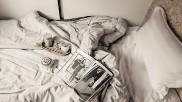 A bed with a magazine, a tray with a cup and jars, and a pillow.
