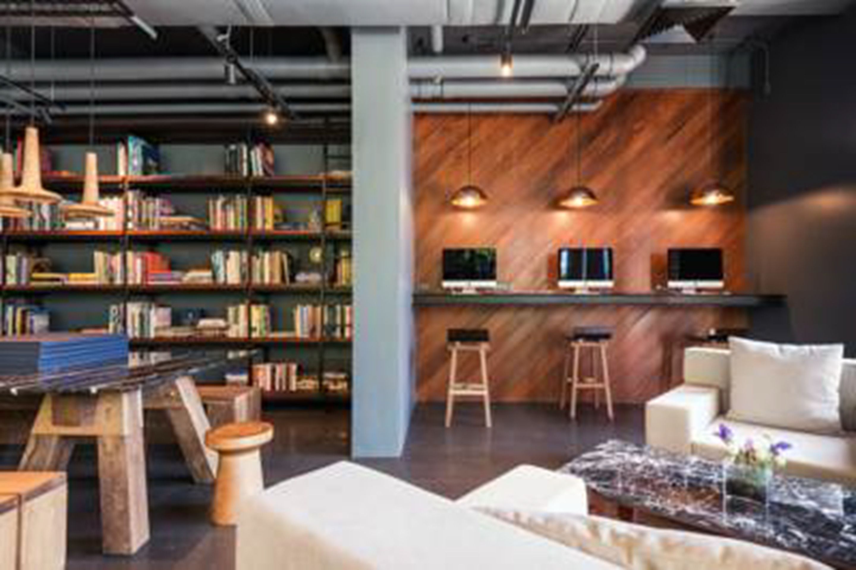 A modern library with bookshelves, a reading area with a sofa and coffee table, and a bar area with stools.