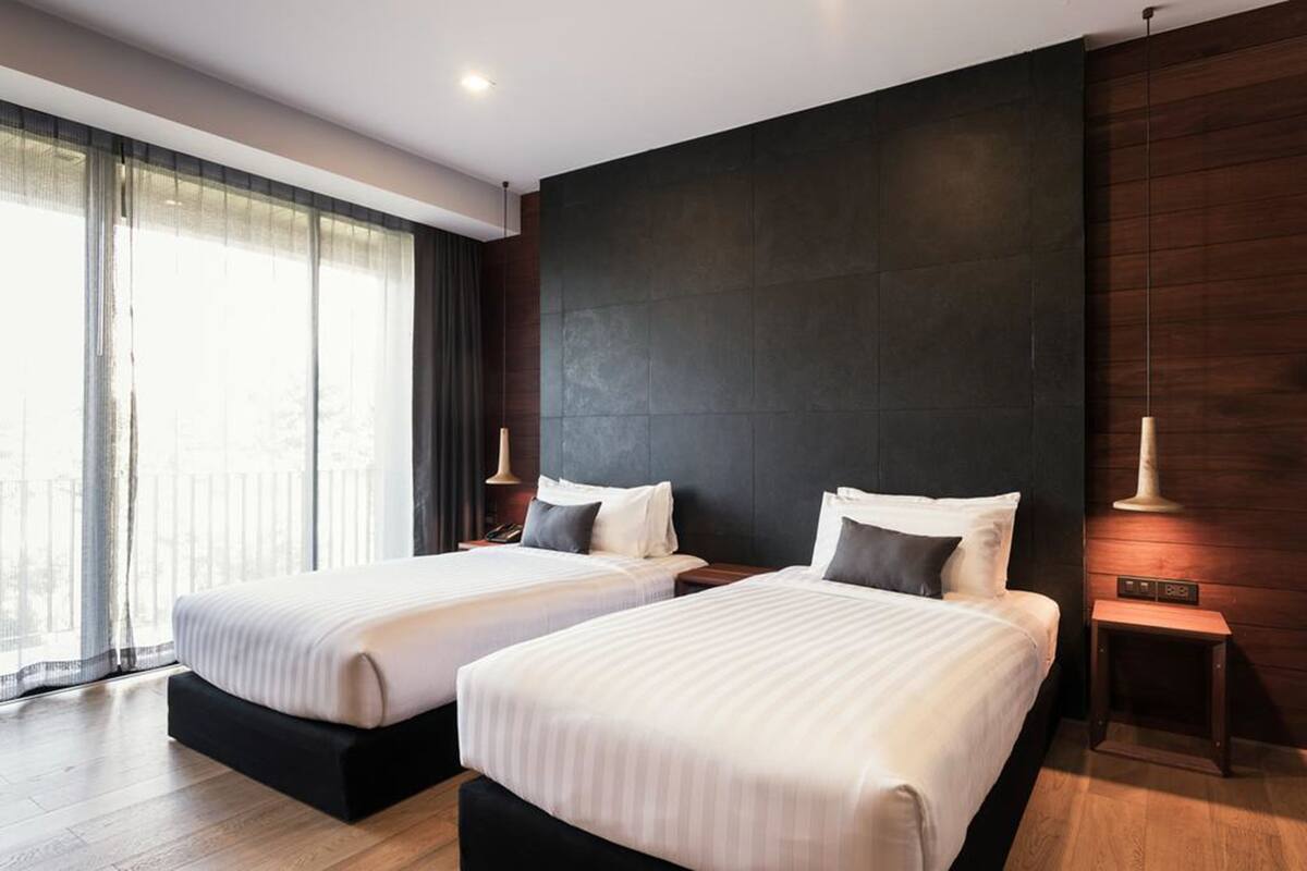 Een hotelkamer met twee bedden, een donkere muur en een groot raam met gordijnen.