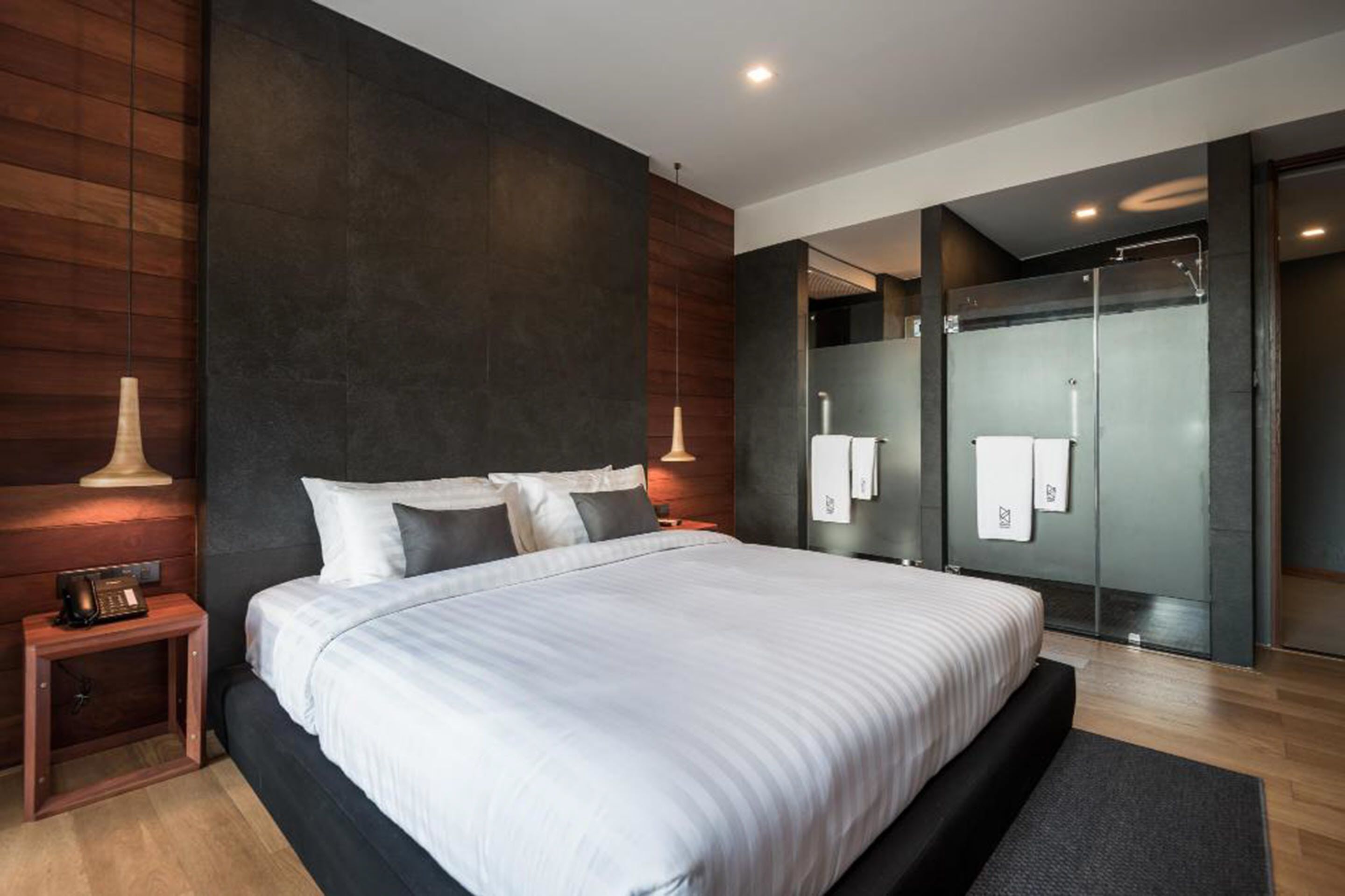 A modern bedroom with a large bed, dark walls, and a wooden floor.