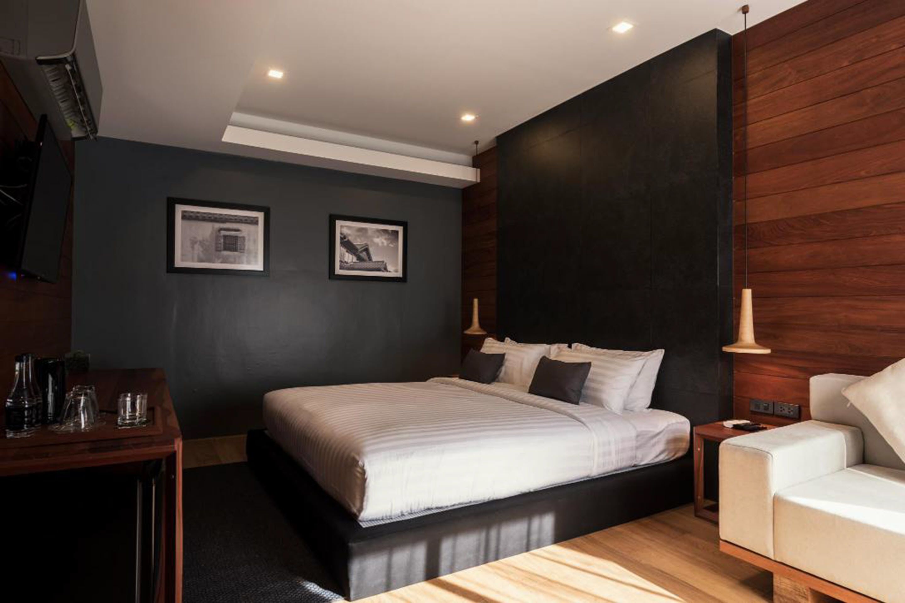 A modern bedroom with a large bed, a wooden nightstand, a bedside table with glasses, and a white sofa.