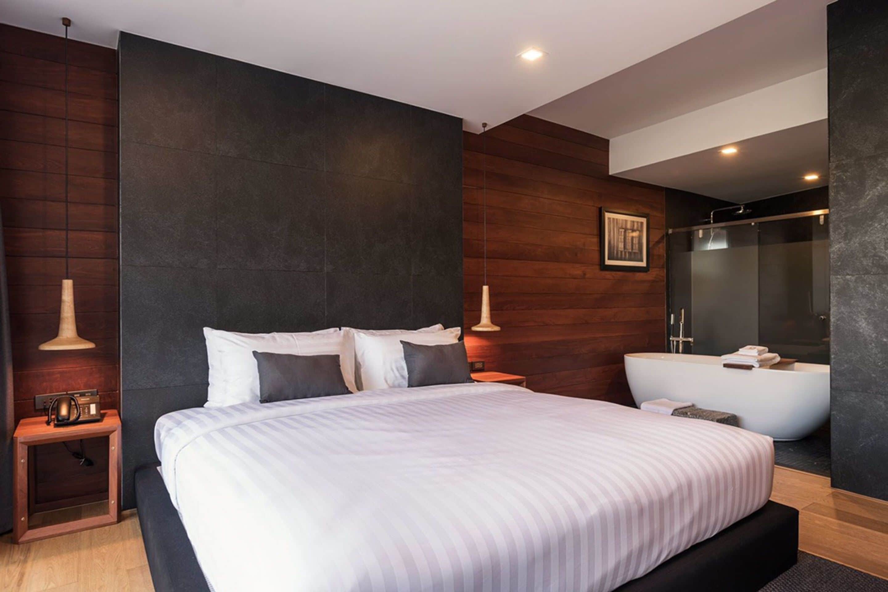 A modern hotel room with a large bed, a separate bathroom with a bathtub, and a wooden accent wall.