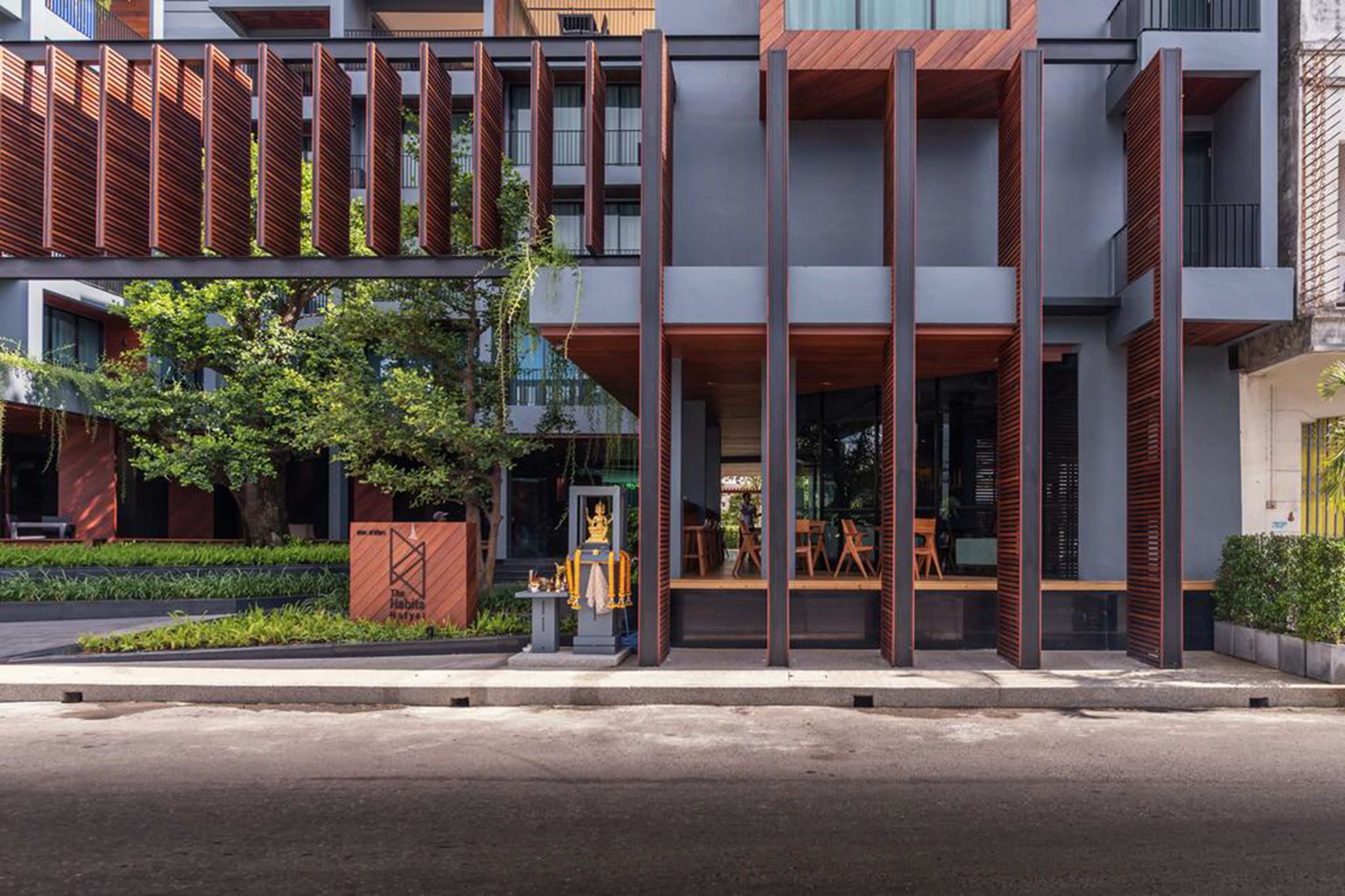 A modern building with a mix of wood and metal exterior, large windows, and a small outdoor seating area.