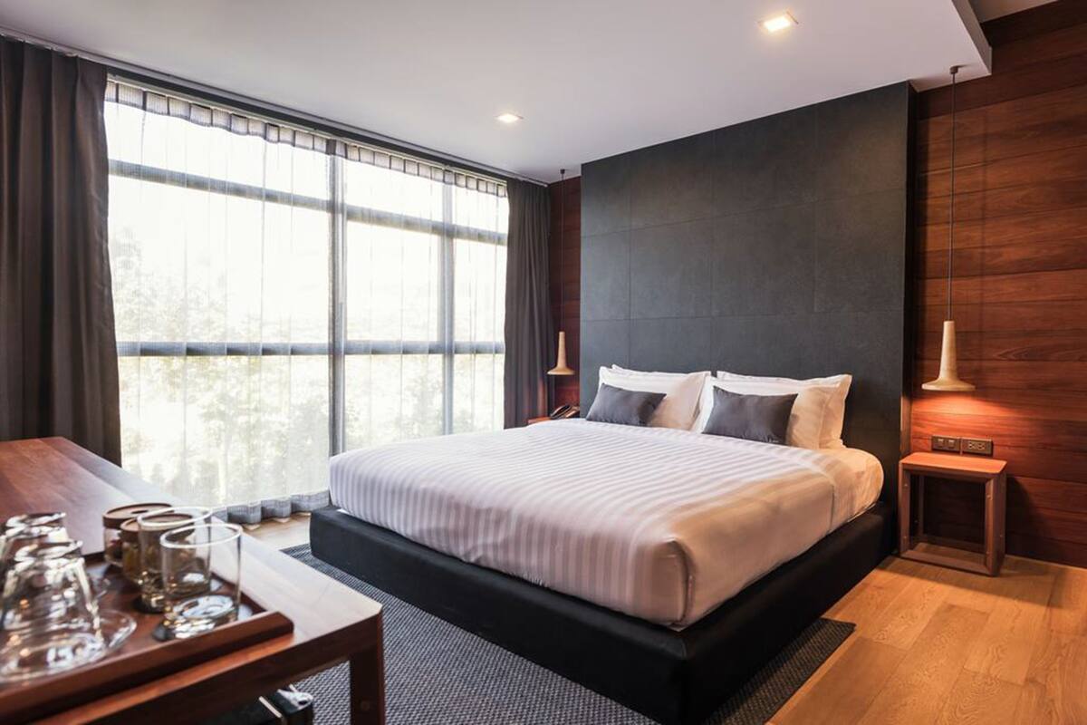 Een moderne hotelkamer met een groot bed, een houten bureau en uitzicht door middel van van top tot teen ramen.
