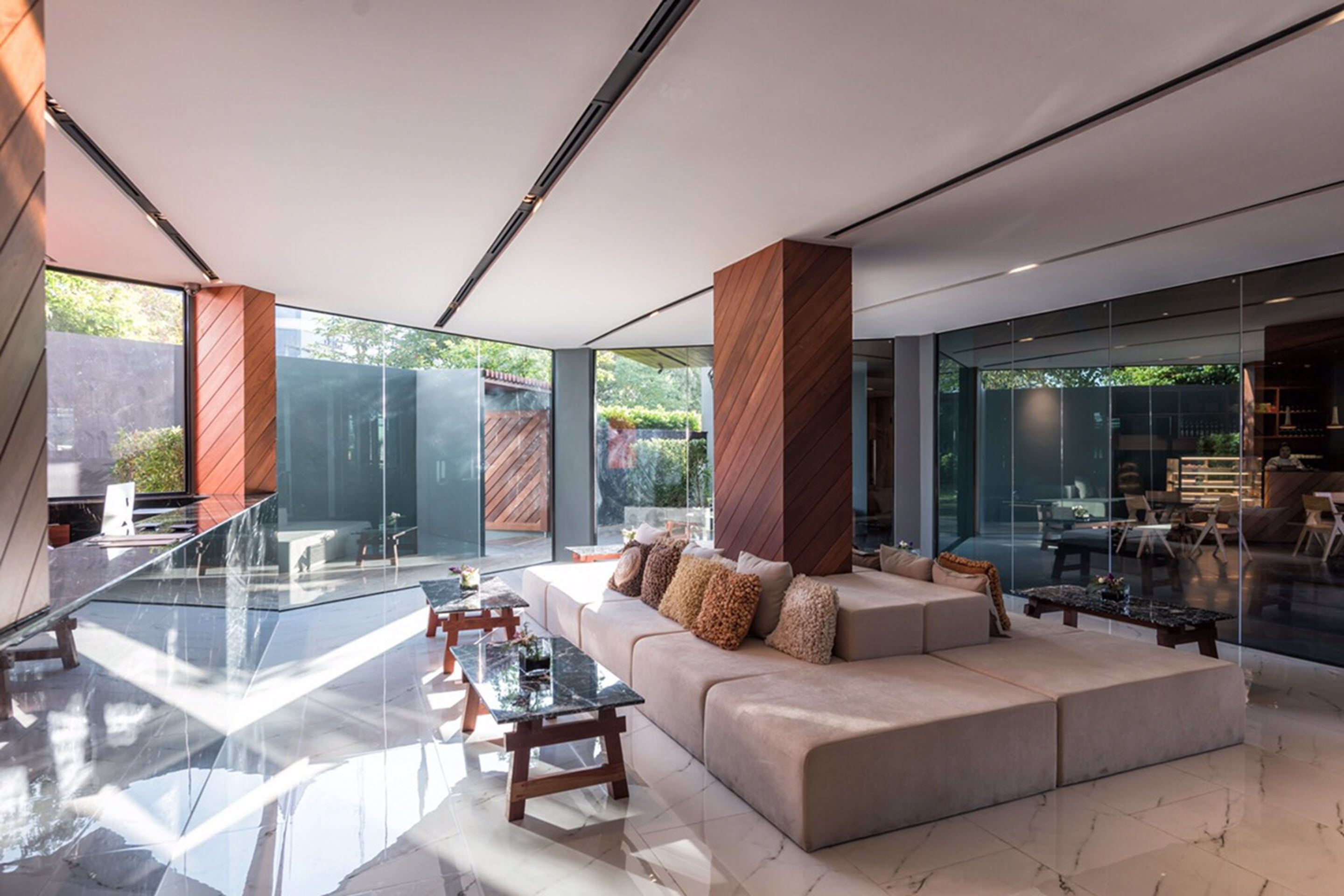 Un interior moderno con una zona de comedor de cristal, un sofá beige con cojines y una pared de acento de madera.
