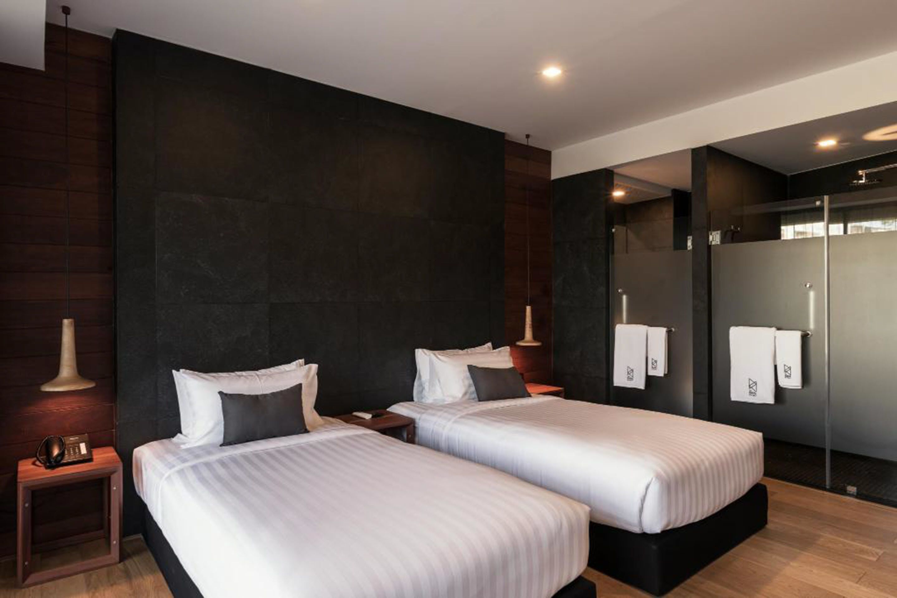 A modern hotel room with two beds, dark walls, and a large mirror.