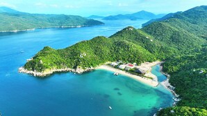 Vista aérea de uma ilha tropical com uma pequena praia, águas azuis cristalinas e vegetação exuberante.
