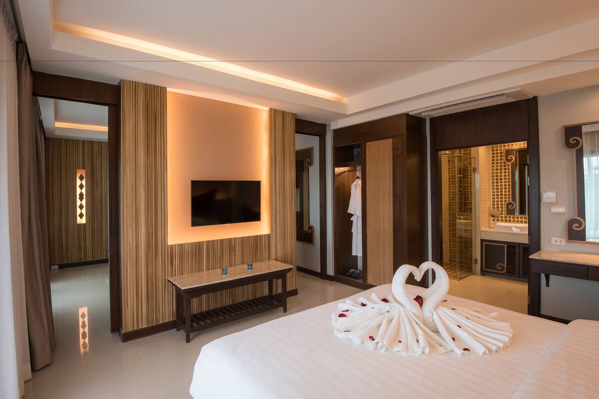 A hotel room with a large bed, a flat-screen TV mounted on the wall, a vanity with a mirror, and a shower area.
