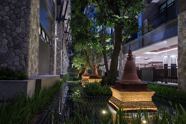 A nighttime view of a courtyard with stone walls, a water feature, and illuminated structures.