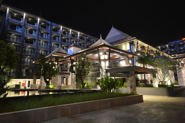 A modern hotel with multiple balconies, a swimming pool, and well-lit outdoor areas.