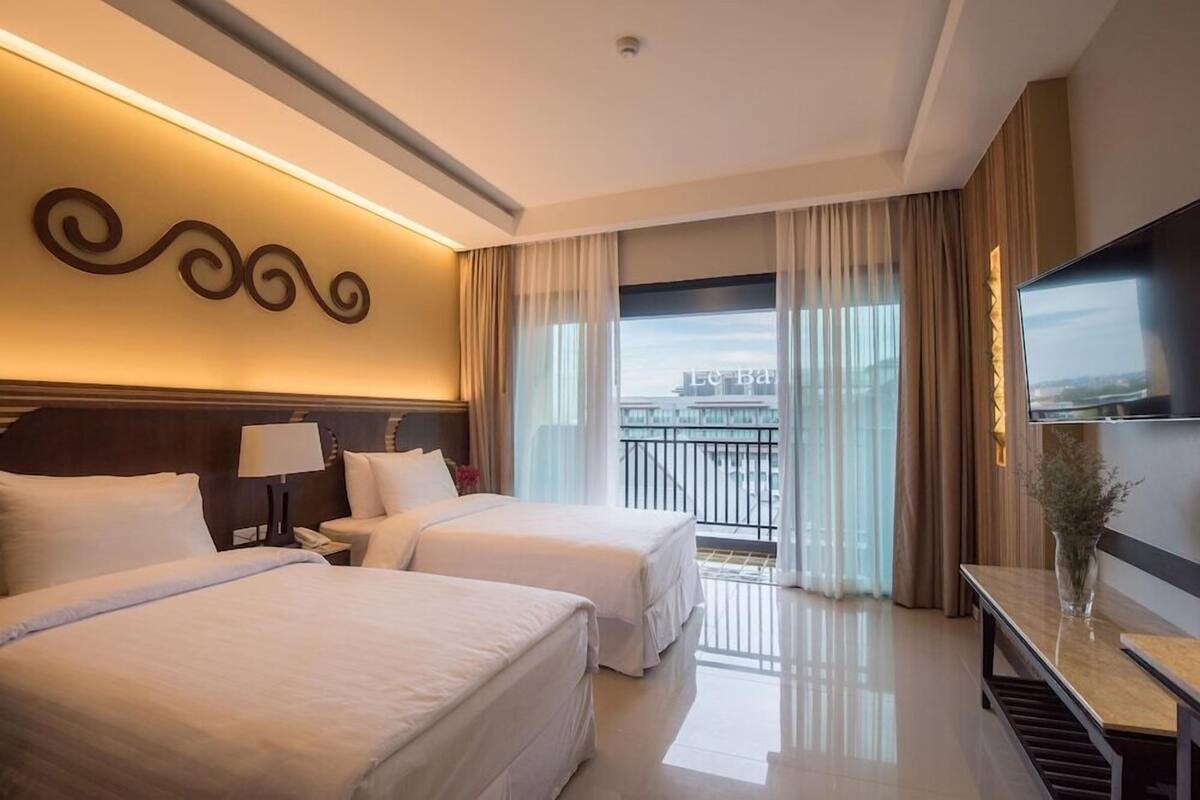 A hotel room with two beds, a TV, a desk, and a balcony with a view.