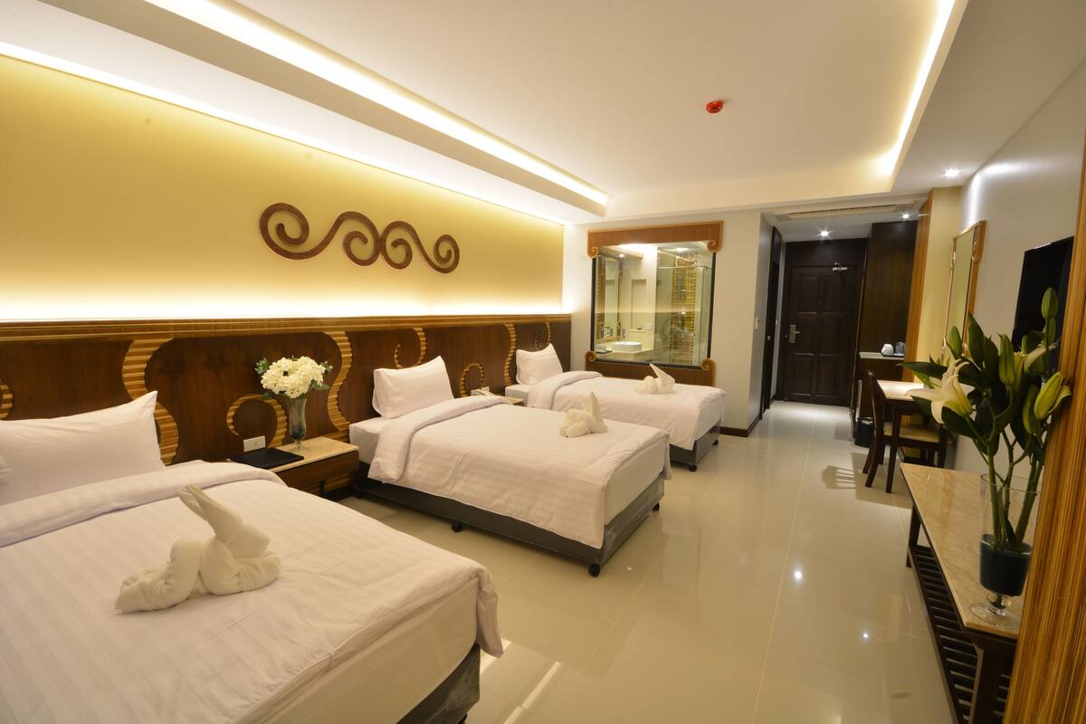 A hotel room with three beds, a bathroom, a dining area, and a large mirror.