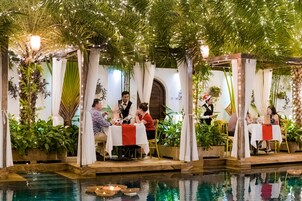 Un comedor interior con mesas dispuestas bajo un toldo de follaje, rodeado por una piscina.