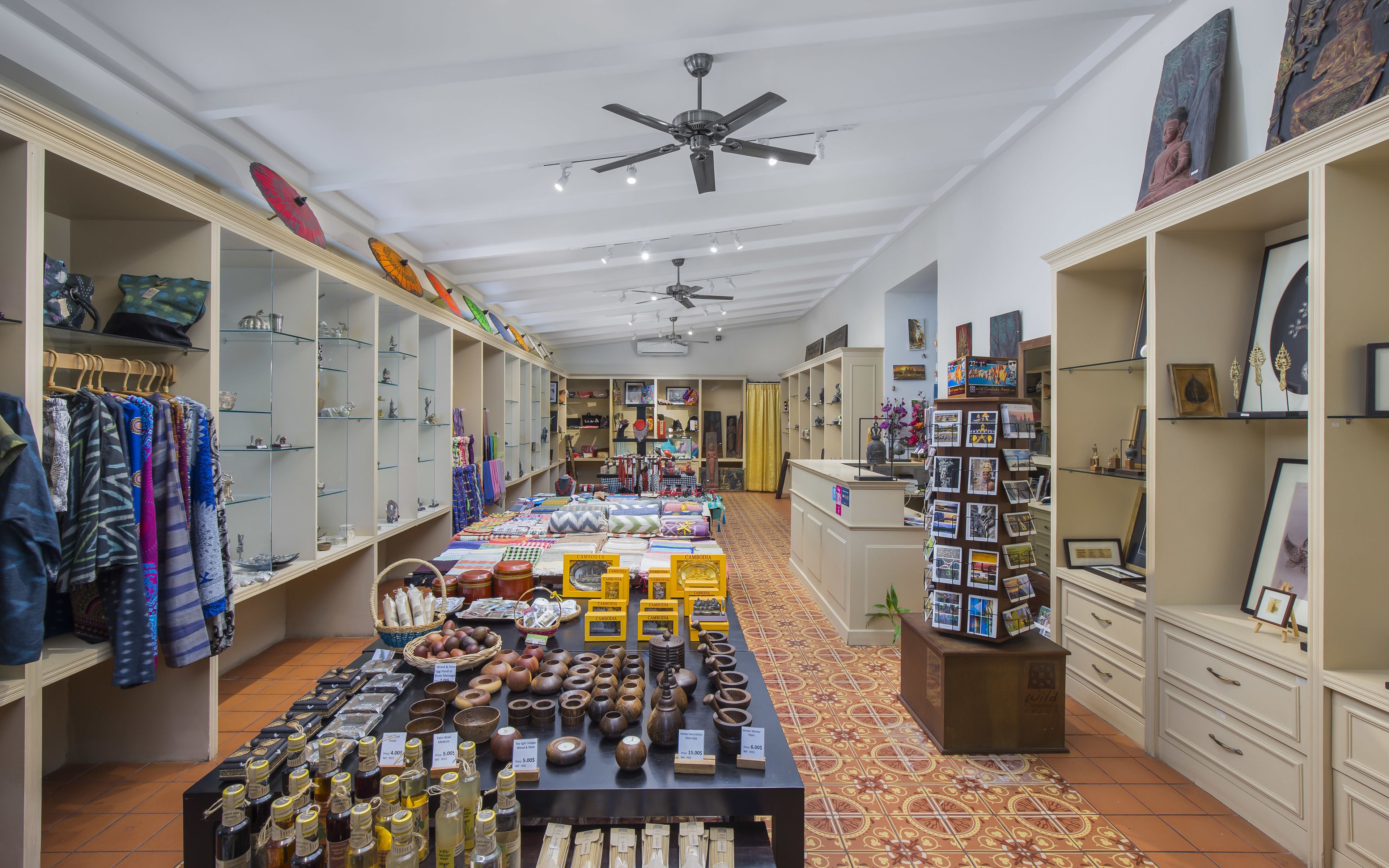 L’intérieur d’un hôtel-boutique présente une pièce maîtresse centrale composée de textiles et de céramiques, encadrée de part et d’autre par des étagères remplies de vêtements et d’objets décoratifs.