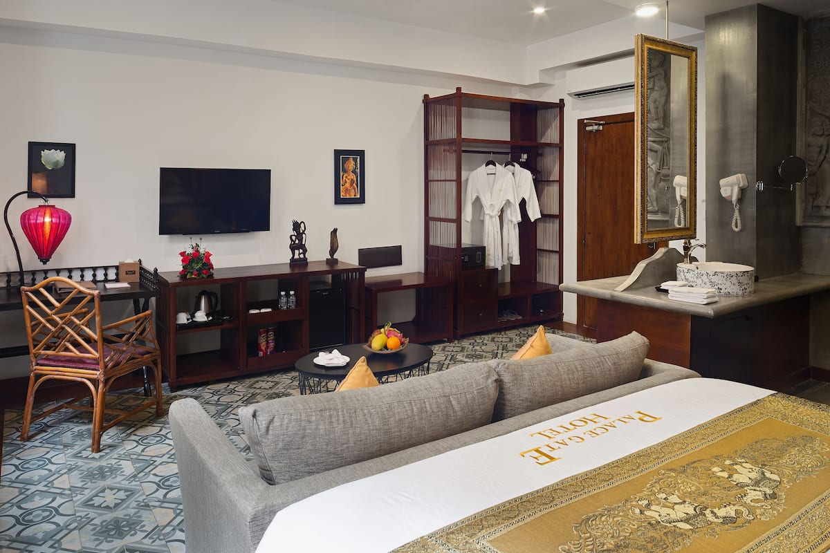 A hotel room with a sofa bed, a TV, a wardrobe, a desk with a chair, a red lantern, and a mirror.