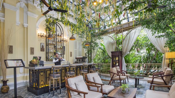 A bar area with wooden furniture, a bar counter, and hanging plants. - Palace Gate Hotel & Resort by EHM (Phnom Penh)