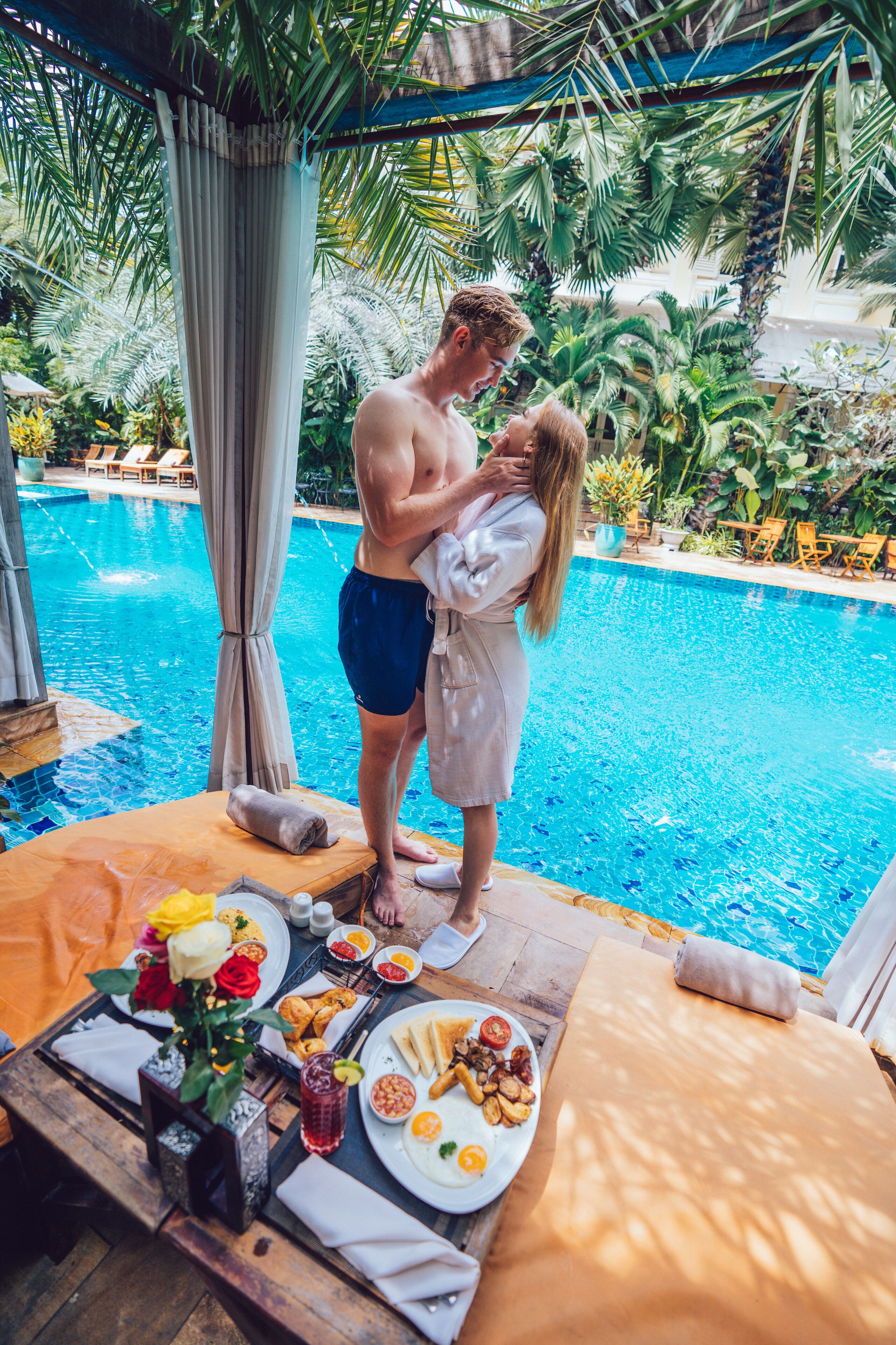 A couple by a pool with a table set for breakfast.