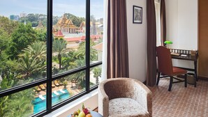 A room with a large window, a chair, a desk, and a small table with fruit. - Palace Gate Hotel & Resort by EHM (Phnom Penh)