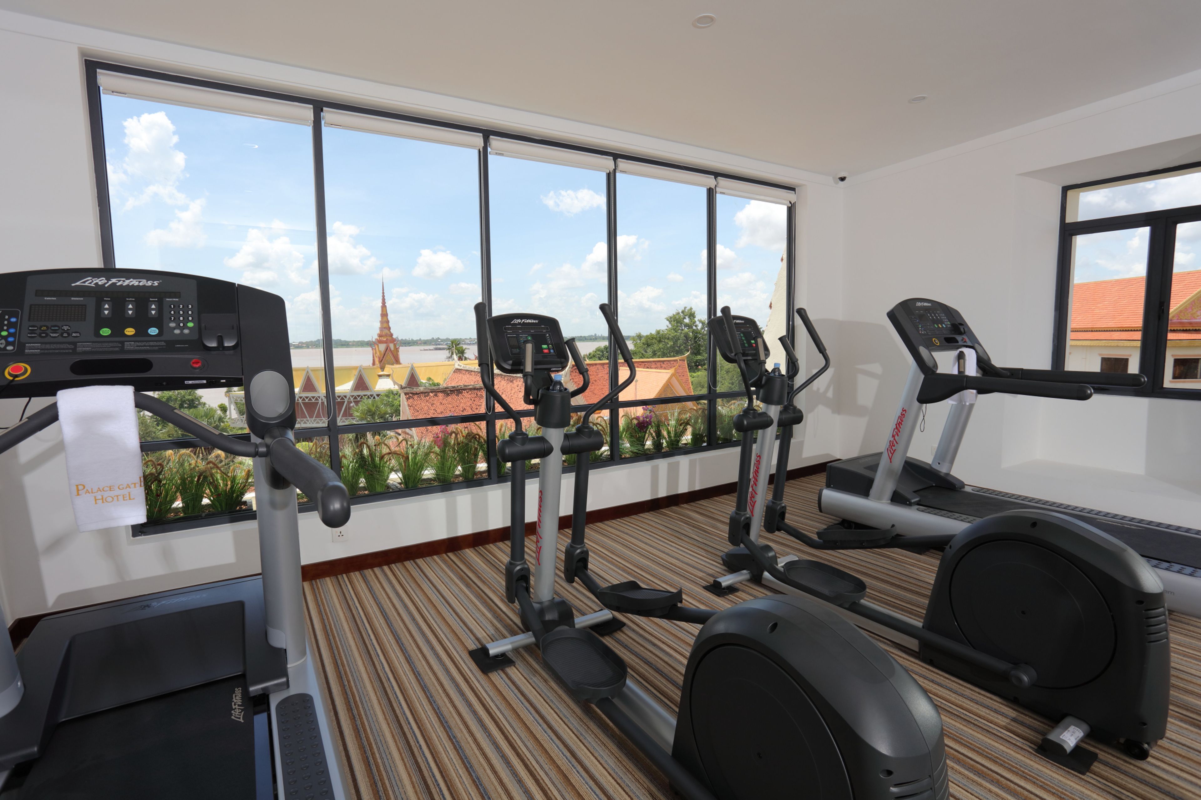 A hotel gym with cardio machines, a large window with a view of a cityscape and a church.