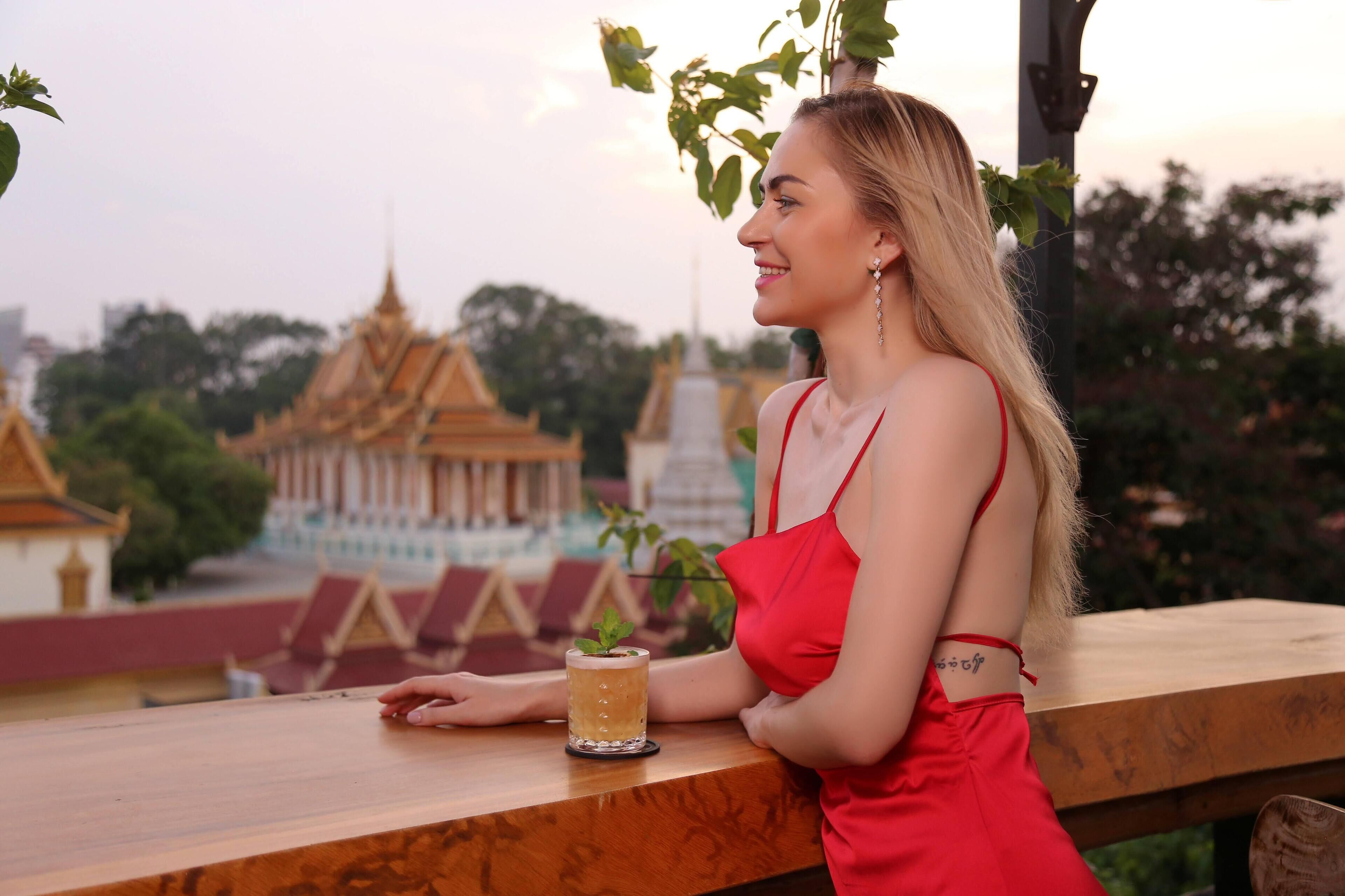 A person sitting at a wooden table with a glass of drink and a plant, overlooking a traditional building with a golden roof.