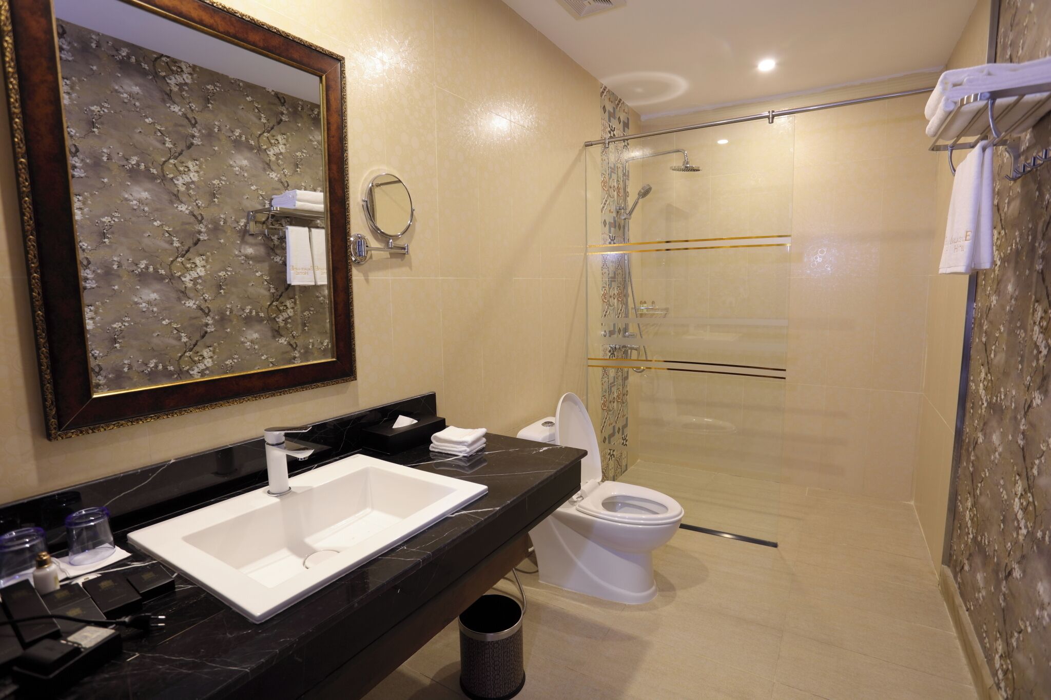 A modern bathroom with a large mirror, a white sink, a toilet, and a glass-enclosed shower.