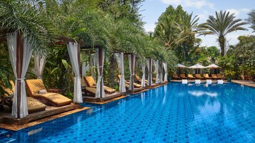 Una piscina con sillas de descanso y sombrillas, rodeada de exuberante vegetación.