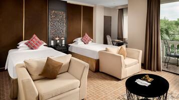 A hotel room with two beds, a sofa, a small table, and a balcony with a view.