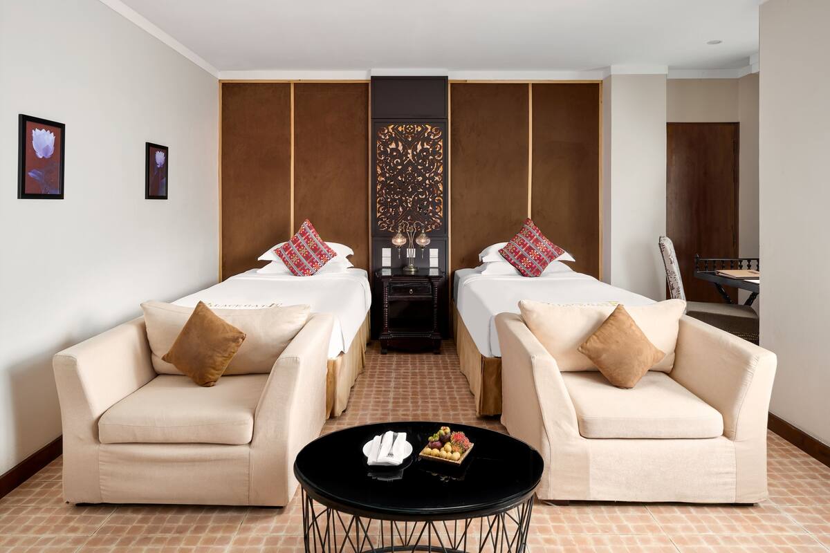 A hotel room with two beds, a sofa, a small table, and a decorative panel.