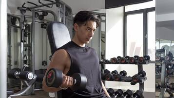 A gym with exercise equipment and a person using a dumbbell.