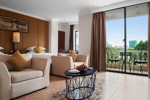 Habitación de hotel con sofá, cama, una mesa redonda con frutero y balcón con mobiliario exterior.