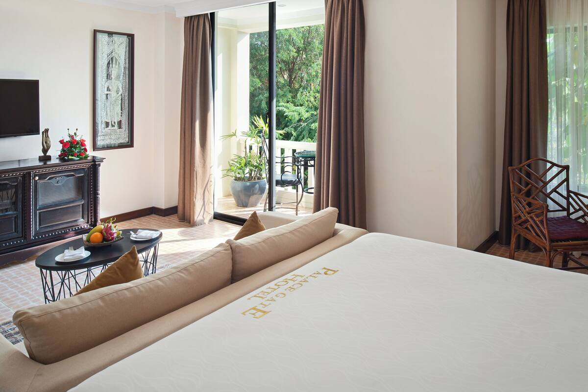 A hotel room with a large bed, a dining table, a TV, and a view of the outdoors.