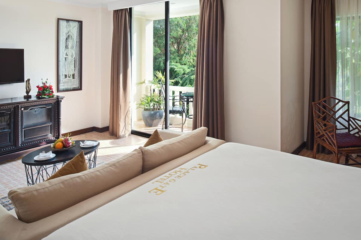 A hotel room with a large bed, a dining table with a fruit bowl, a television, and a view of the outdoors.