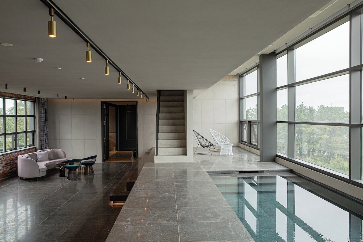 A spacious lobby with a modern staircase, a seating area with sofas and chairs, and large windows offering a view of the outdoors.