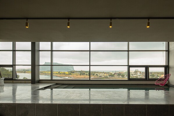A spacious room with large windows, a pool, and a view of a distant landscape. - Playce Camp Jeju (Seogwipo)