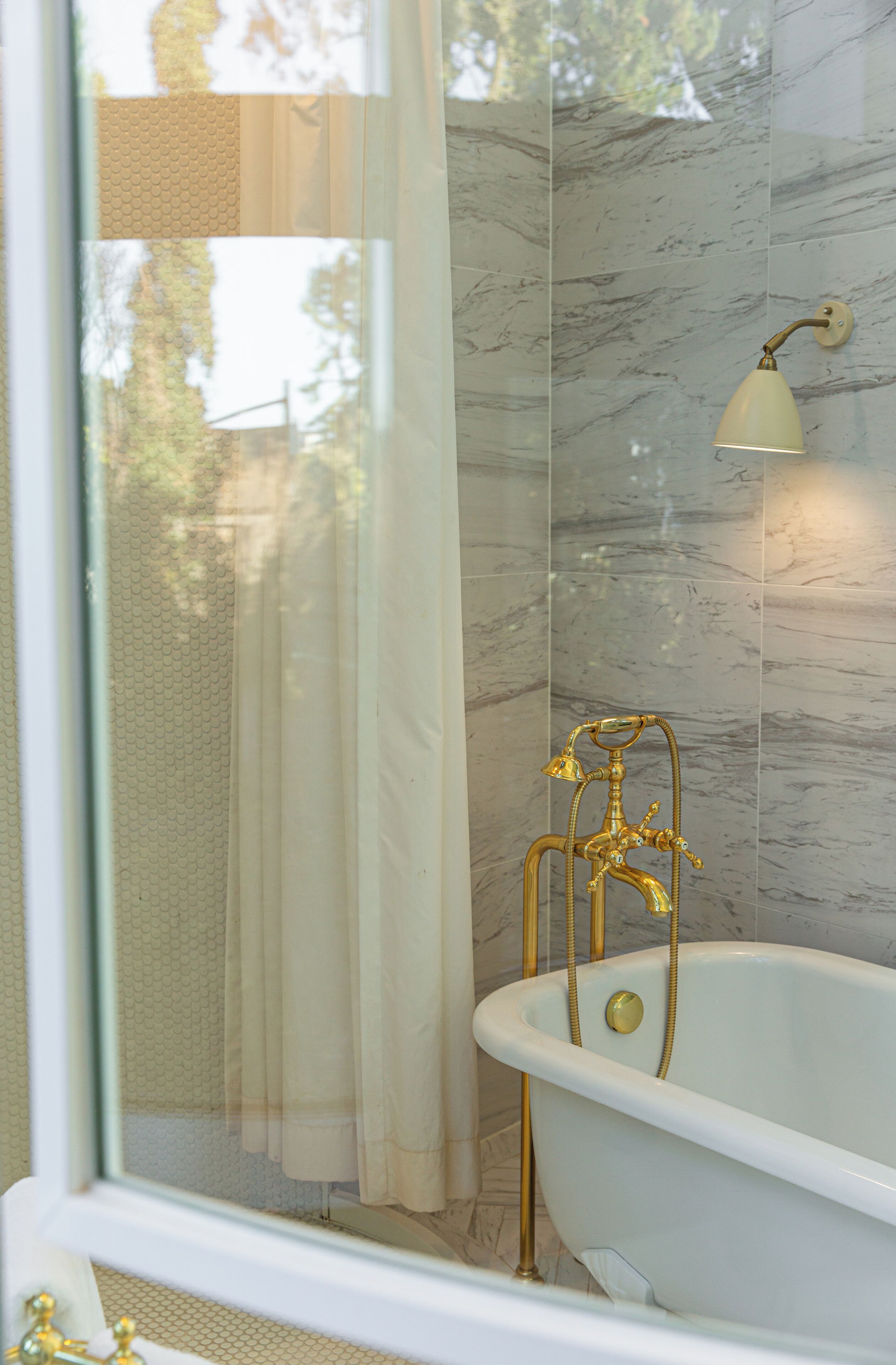 A bathroom with a freestanding bathtub, marble walls, and a window with a view of trees.