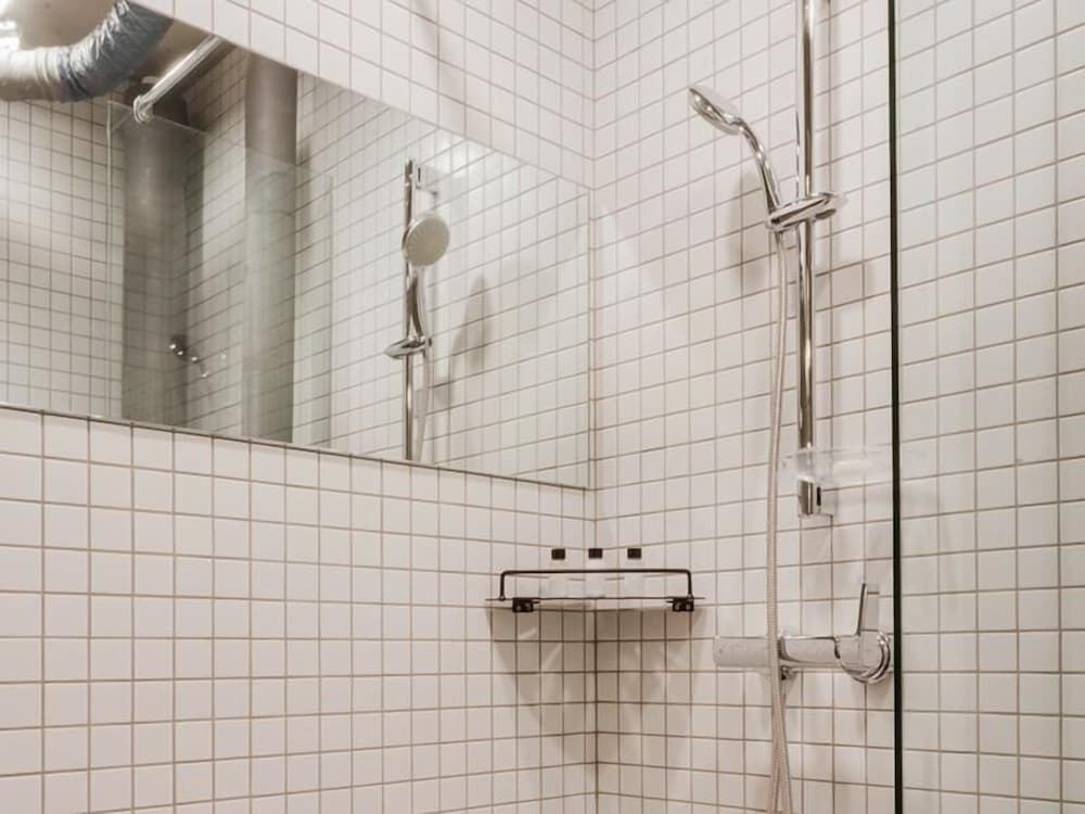 Ein Badezimmer mit weißen Fliesen, einem Spiegel, einer Dusche mit Duschhandstück und einem Handtuchhalter.