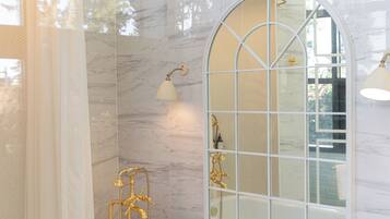 A bathroom with a bathtub, gold fixtures, and a large arched window.
