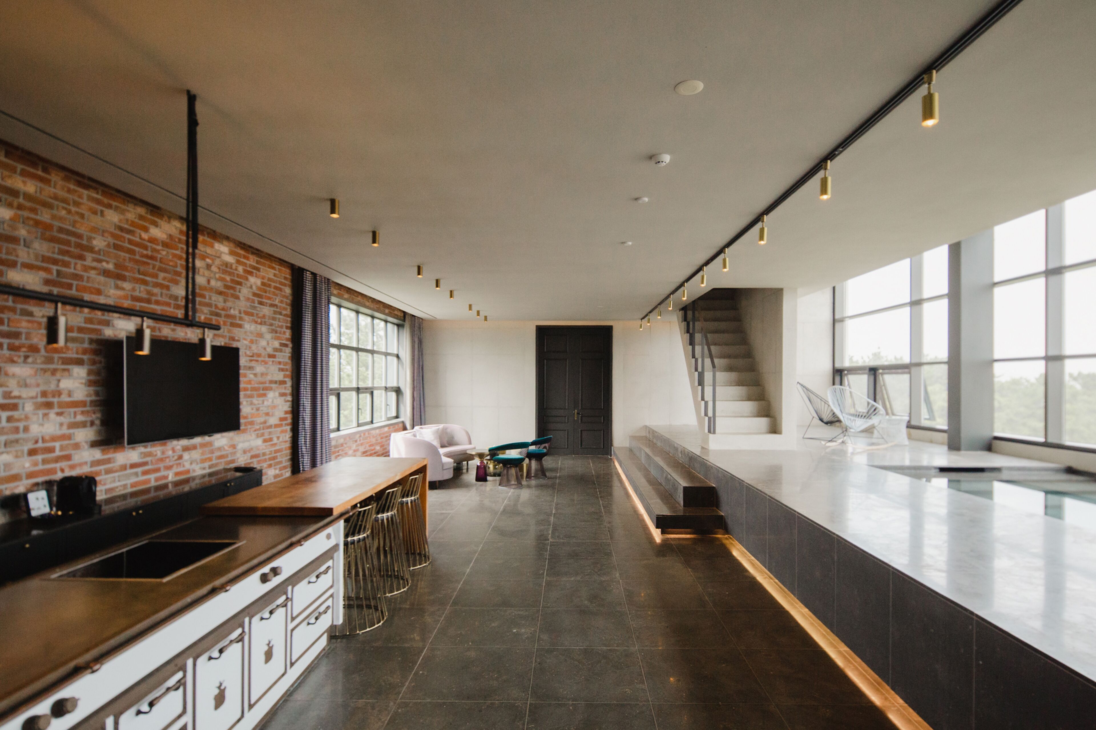 A modern kitchen with a brick wall, a large island with bar stools, and a staircase leading to a balcony.