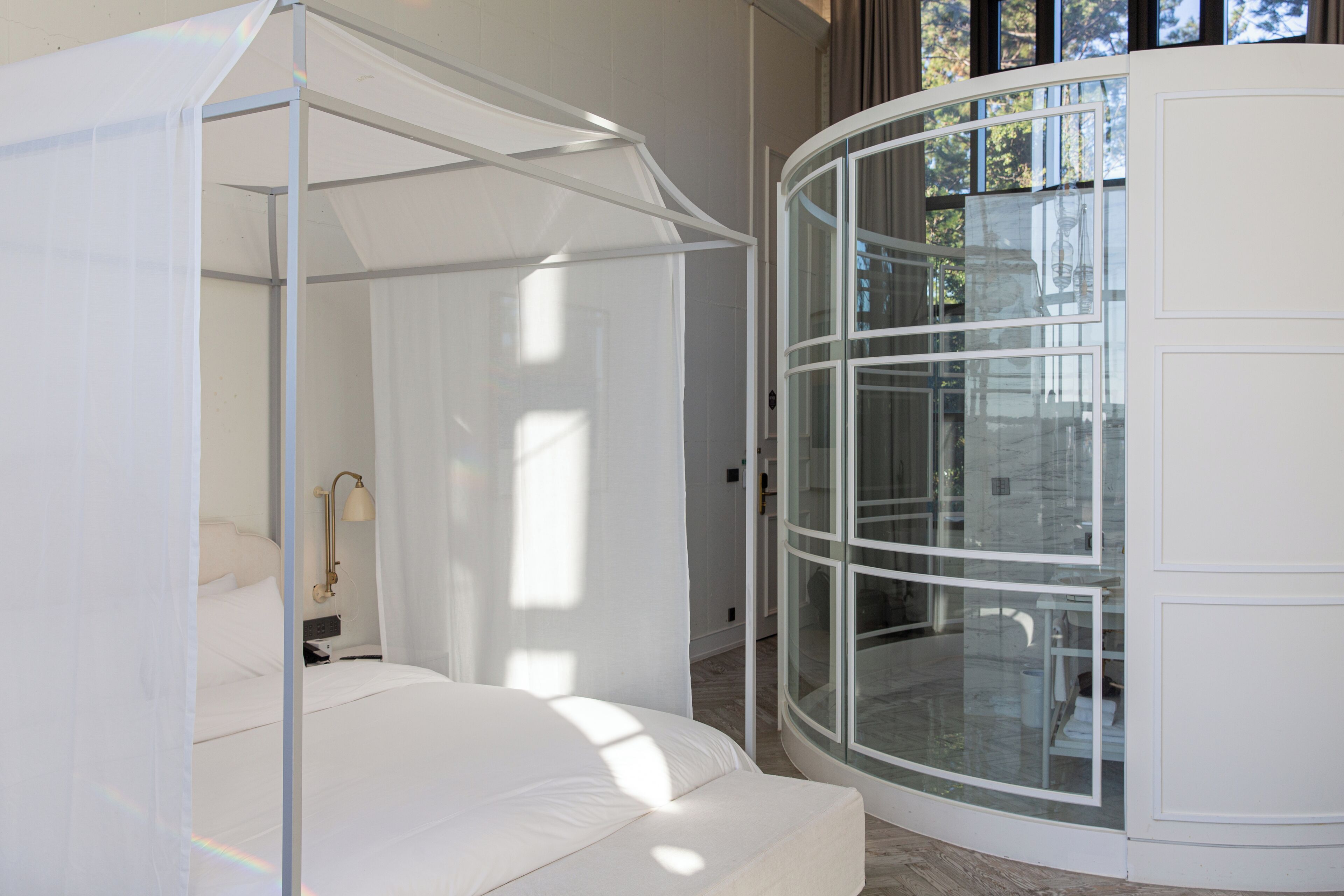 A modern bedroom with a canopy bed, a glass door, and a view of the outdoors.