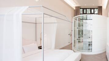 Quarto moderno com cama de dossel, poltrona giratória com estrutura de vidro e vista para o exterior através de uma janela.