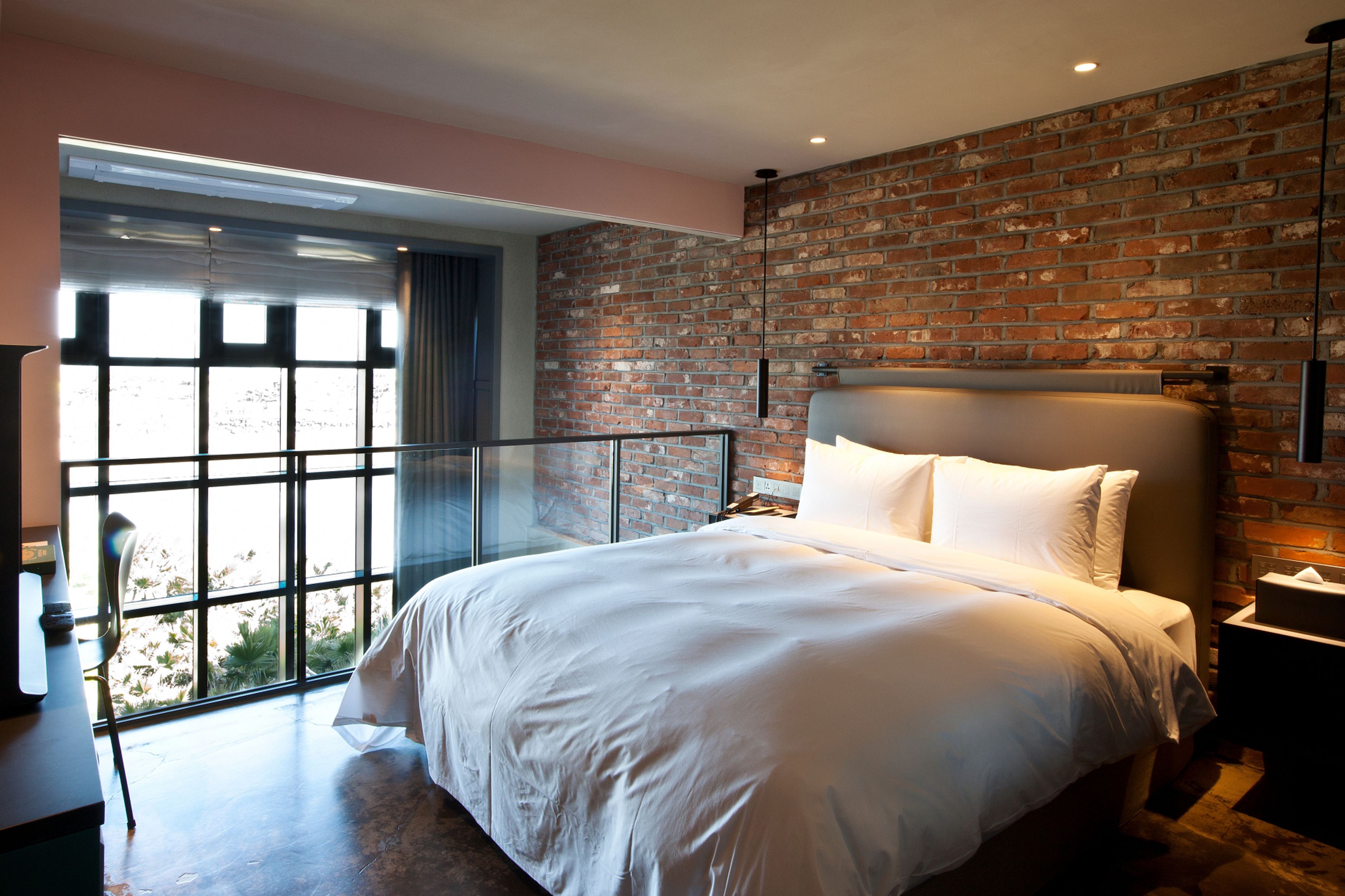 Une chambre moderne avec un grand lit, un mur en briques et un balcon offrant une vue dégagée.