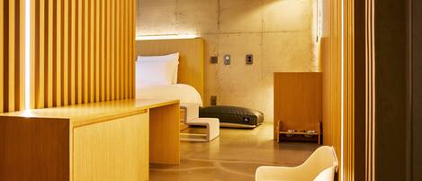 Ein modernes Hotelzimmer mit einem Bett, einem Holztisch, einem Stuhl, einer kleinen Couch und einem Schlafplatz für Haustiere.