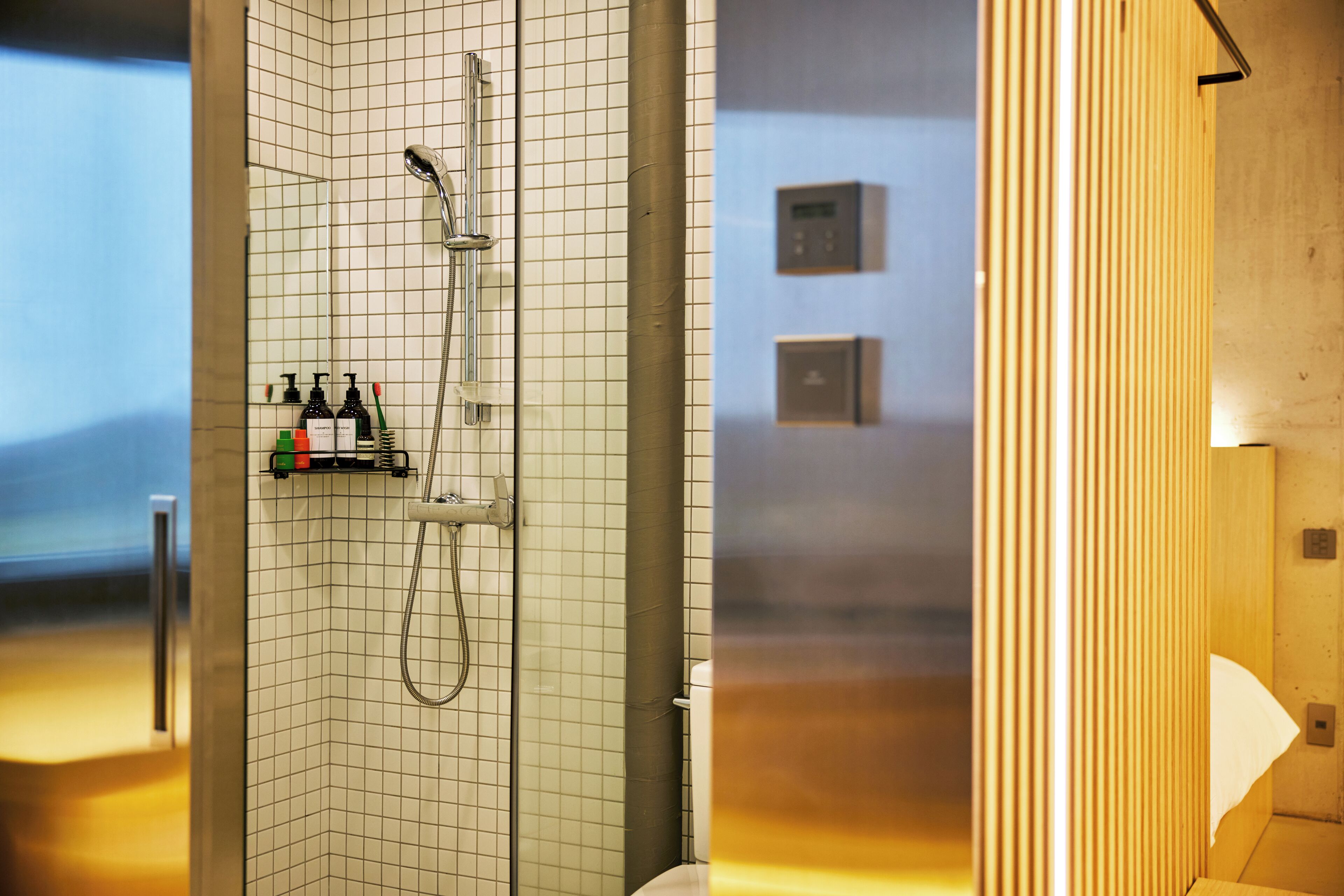 A modern bathroom with a grid-patterned shower wall, a handheld showerhead, and a shelf with toiletries.