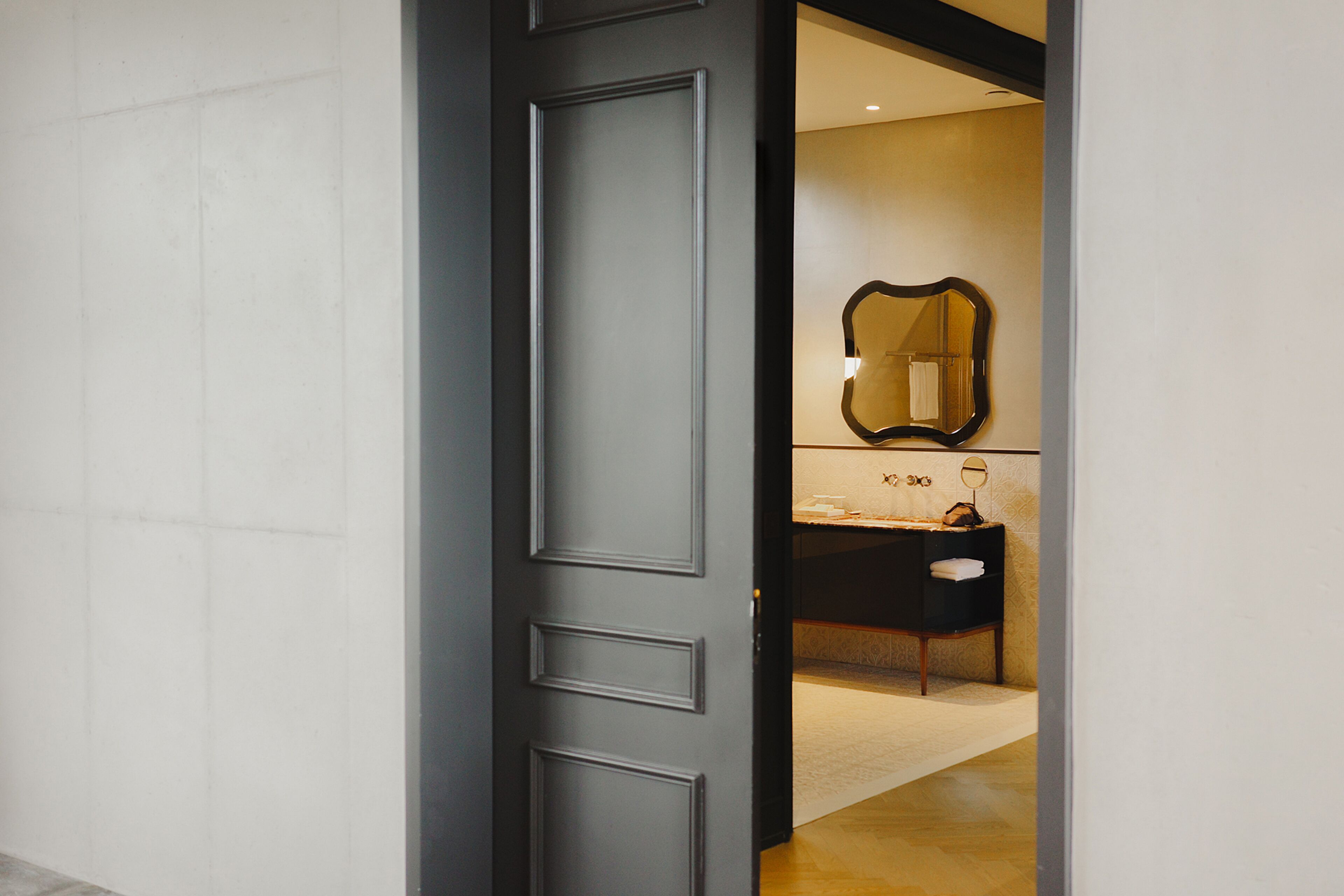 Un baño moderno con una puerta de madera oscura, un espejo grande y un lavabo blanco.