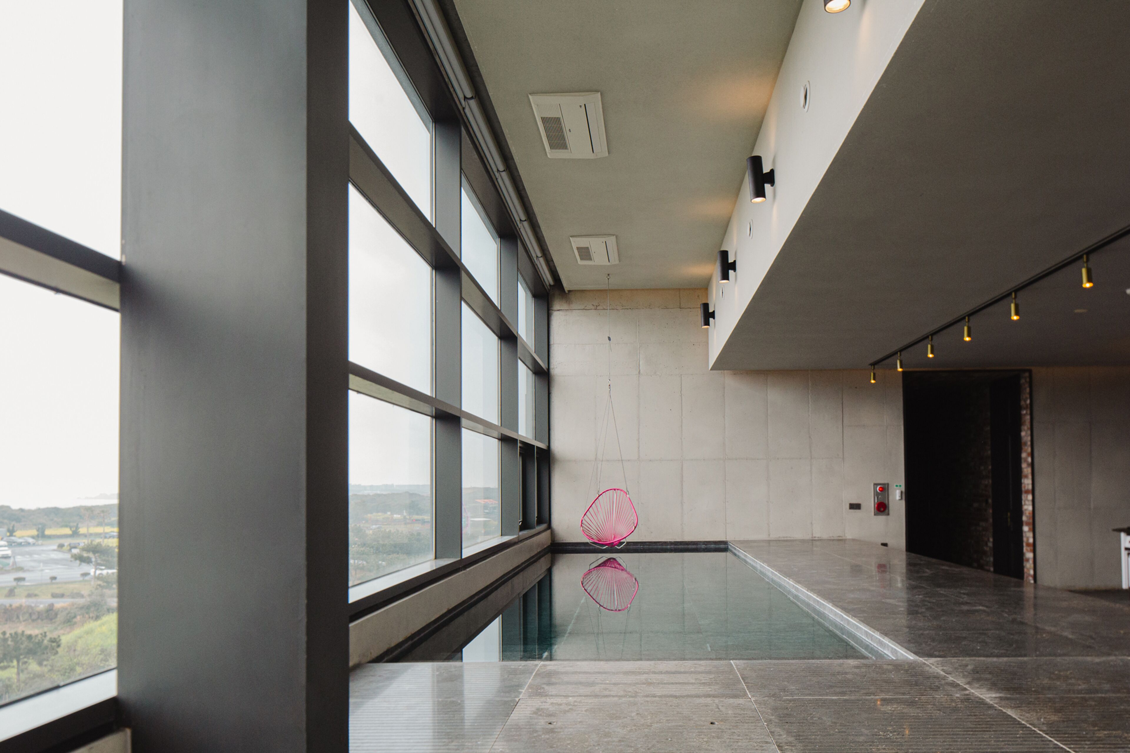 Un espace piscine intérieur moderne, doté de grandes fenêtres offrant une vue dégagée sur l’extérieur et d’un design minimaliste.