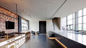A modern kitchen with a brick wall, a large window, and a staircase leading to an upper level. - Playce Camp Jeju (Seogwipo)