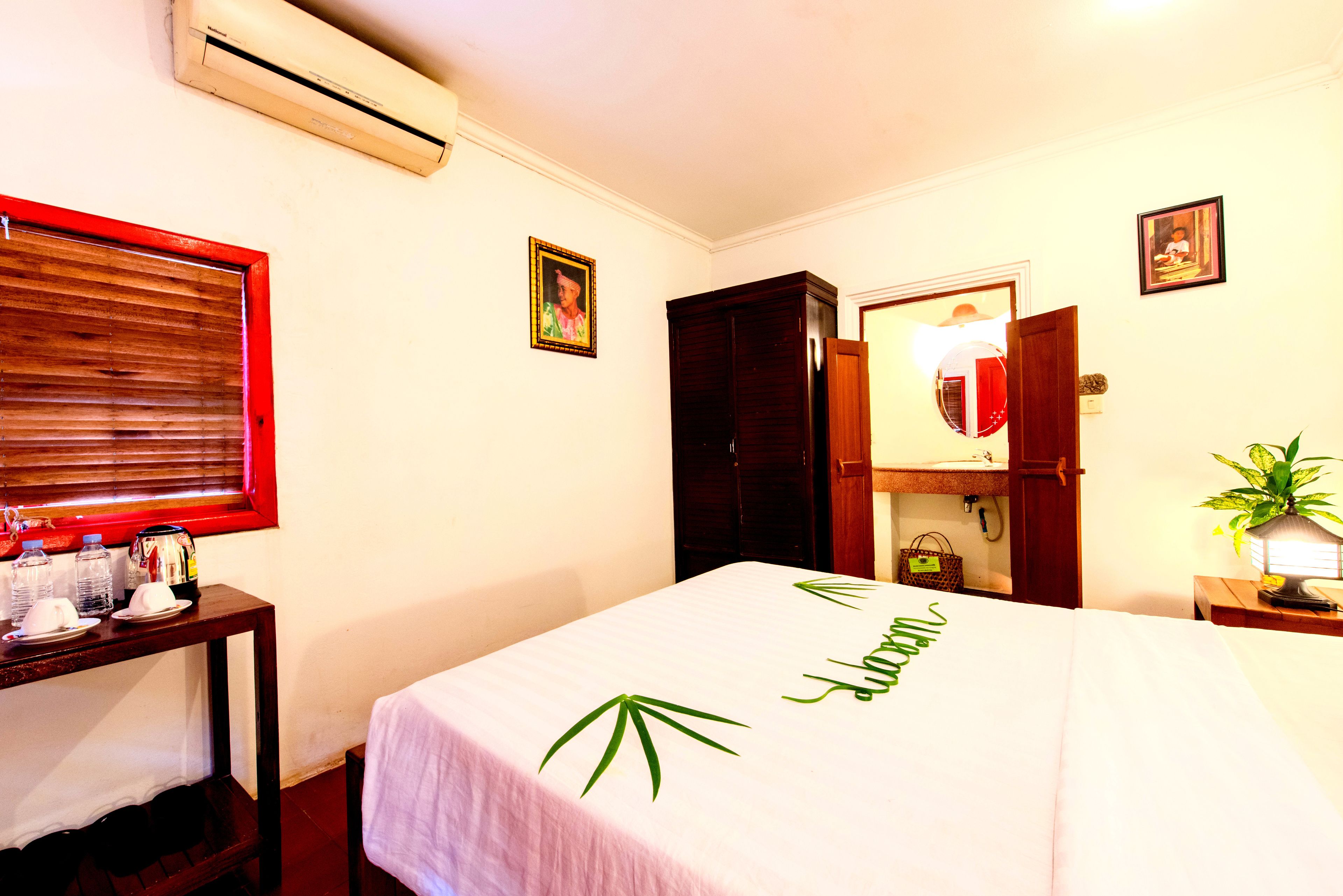 Una habitación de hotel con cama, una mesa con hervidor, una planta y un espejo.